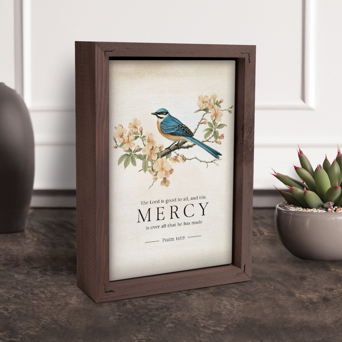 Decorative frame with a bird illustration and 'Mercy' text on a table with a plant in the background | InsideOutCatalog.com