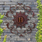 Monogrammed Iron Wall Grille - Monogram Wall Decor | Estate Quality Home Decor | Personalized Wall Decor | Shown with the Monogram "H" | Iron finished in a rustic brown-gold stain with Italian gold 5" monogram shown on grey stone wall with greenery | INSIDE OUT | InsideOutCatalog.com