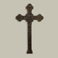 A large wall-mounted iron cross with intricate designs, finished in brown taupe, displayed against a plain background.