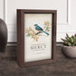 Decorative frame with a bird illustration and 'Mercy' text on a table with a plant in the background | InsideOutCatalog.com