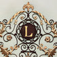 Monogrammed Iron Wall Grille - Palace Inspired Personalized Wall Decor (49.75"W) | Estate Quality Home Decor | Personalized Wall Decor | Shown with the Monogram "L" | Iron finished in a rustic brown and antique gold stain with Italian gold 5" monogram (close up of monogram letter) | INSIDE OUT | InsideOutCatalog.com