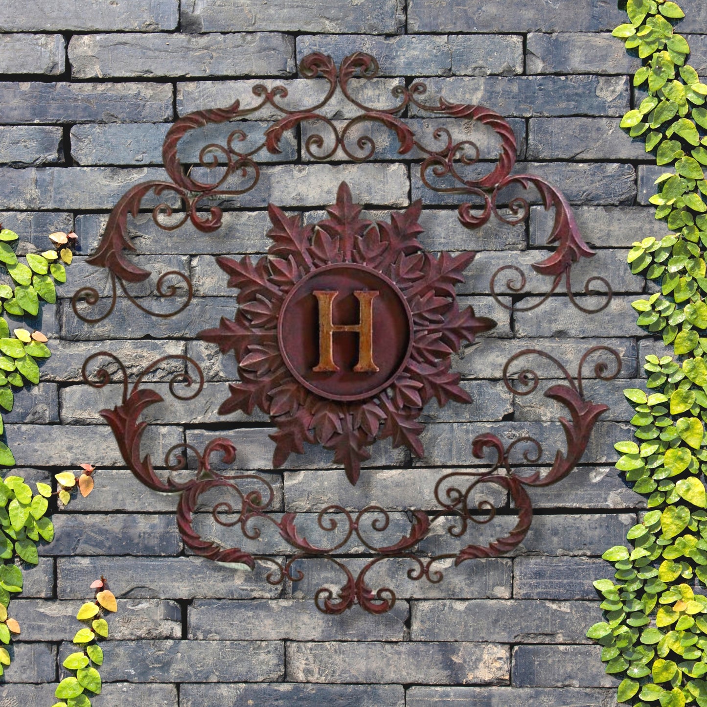 Monogrammed Iron Wall Grille - Monogram Wall Decor | Estate Quality Home Decor | Personalized Wall Decor | Shown with the Monogram "H" | Iron finished in a rustic brown-gold stain with Italian gold 5" monogram shown on grey stone wall with greenery | INSIDE OUT | InsideOutCatalog.com